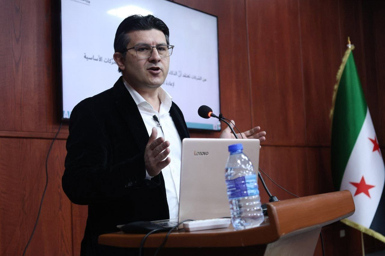 Dr Fadi Amroush delivering a lecture at a lectern, with presentation slides behind him