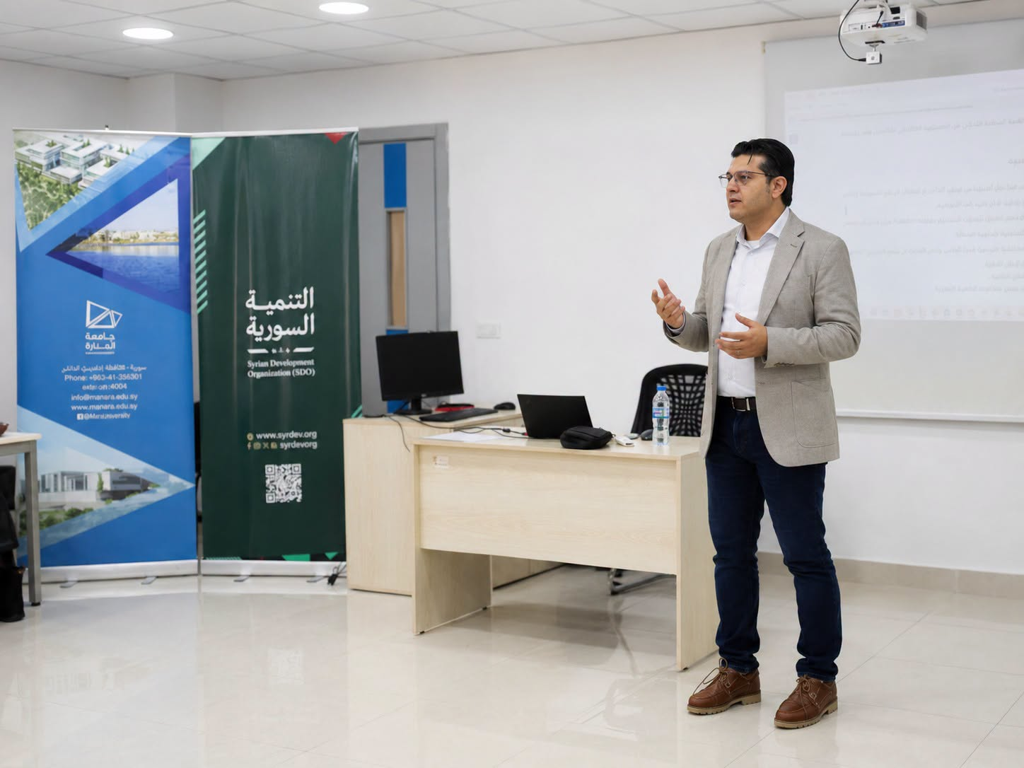 Dr Fadi Amroush leading a training session with Manara University and Syrian Development Organization banners in the room